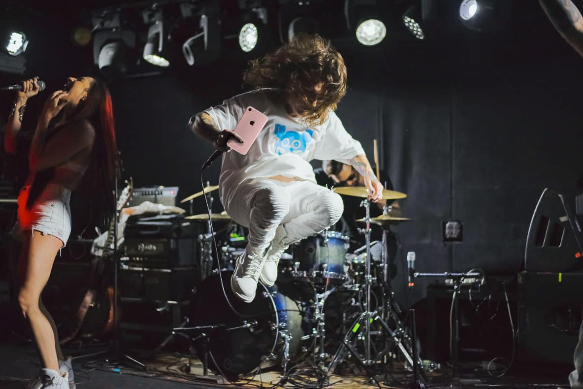 Rock concert with dude holding a pink mobile phone while jumping